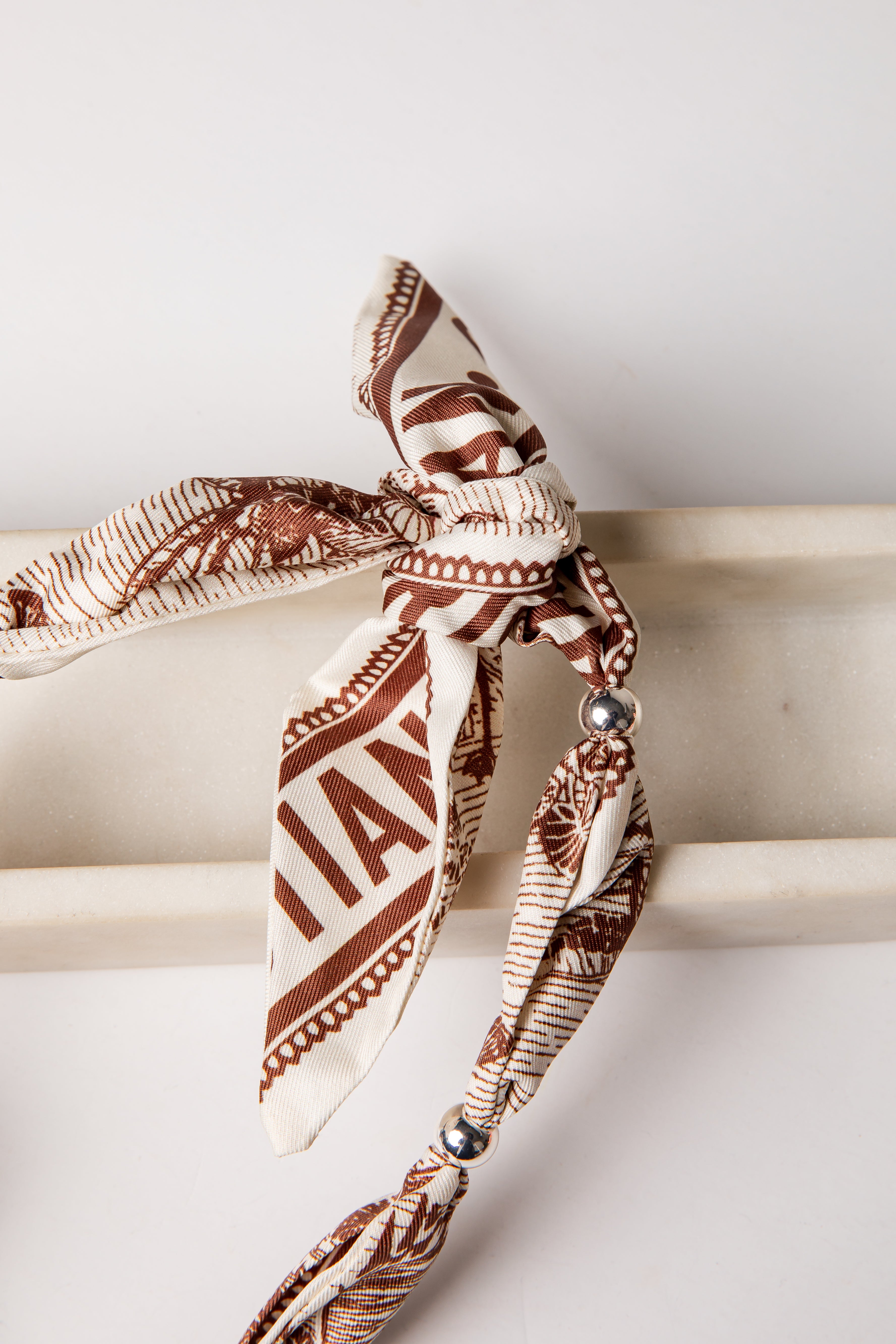 Brown and beige patterned headband with decorative elements on a white surface