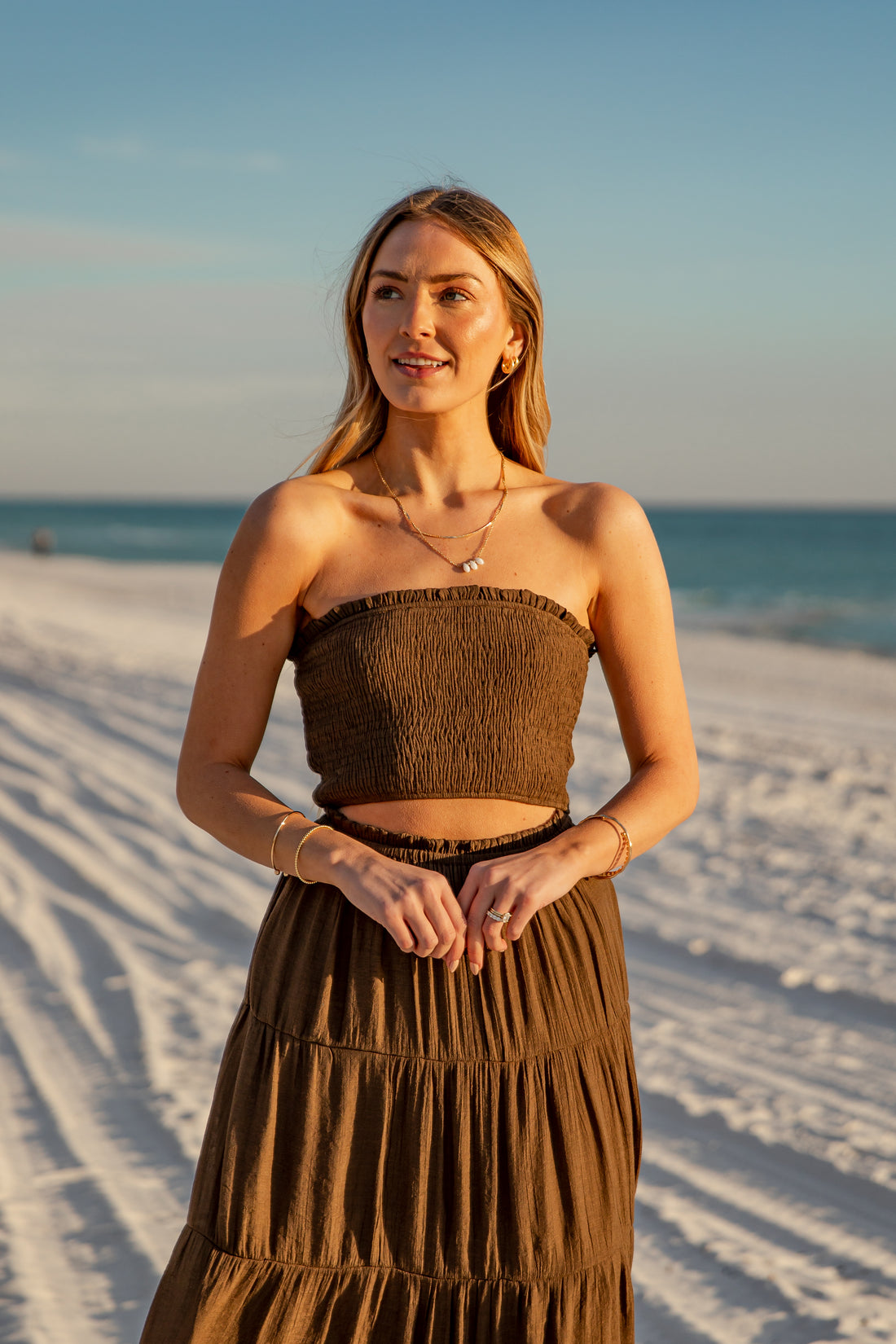 Woman in a brown dress standing on a sandy beach with ocean in the background