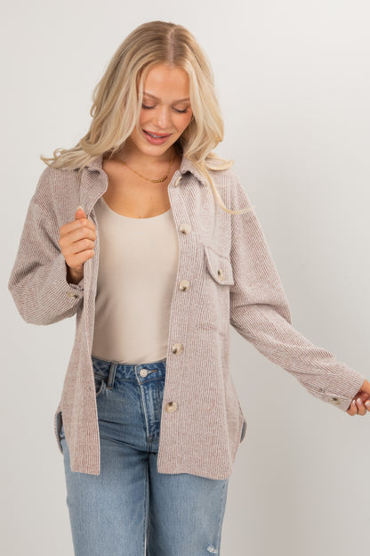 Woman wearing a beige cardigan over a white top and blue jeans on a plain background