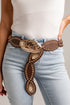 A close-up of a person wearing a brown leather western belt with large engraved gold-toned medallions and silver-tone studs, paired with light blue jeans and a white top.