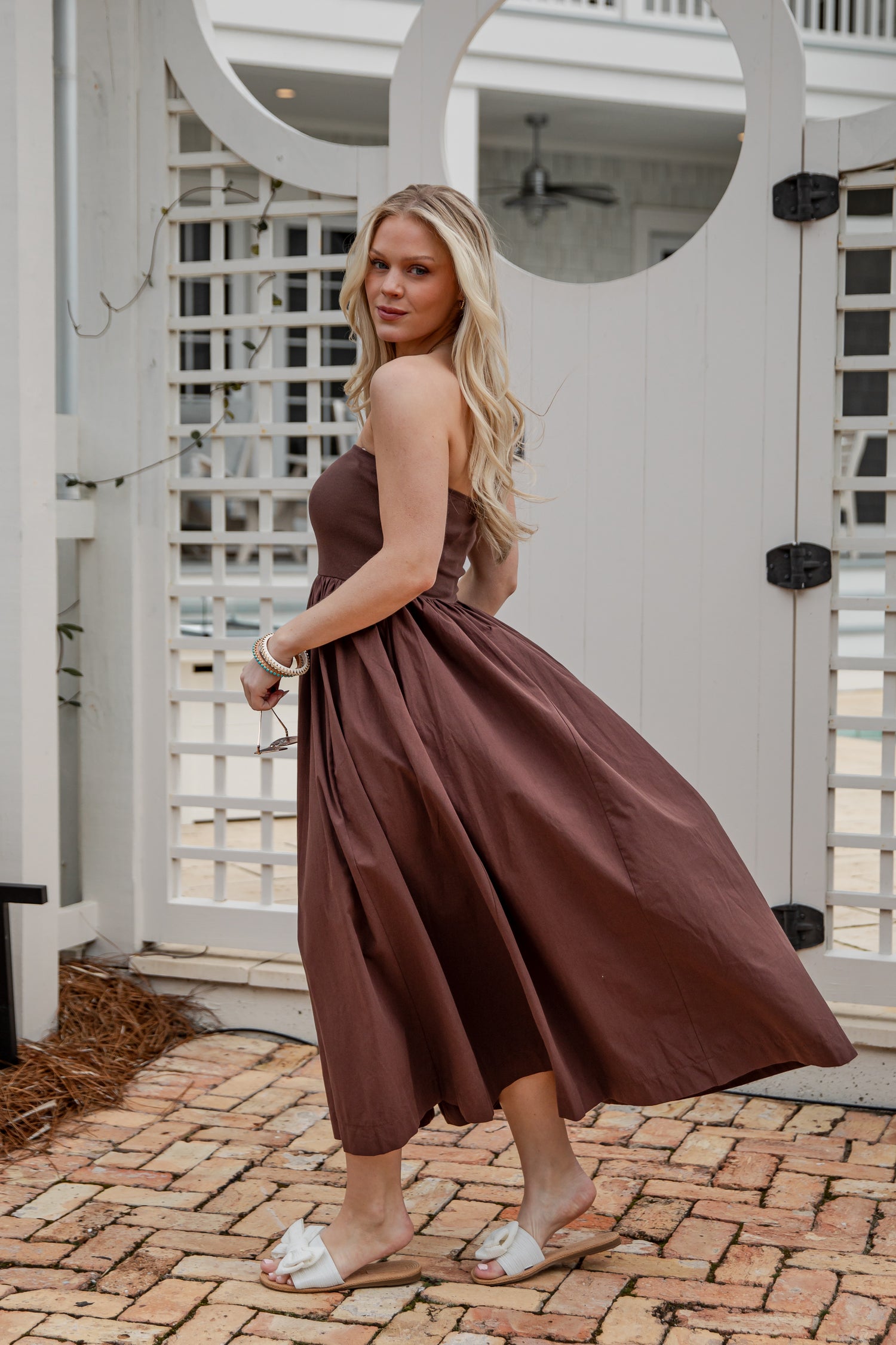Woman in a brown dress standing on a brick patio with white lattice background