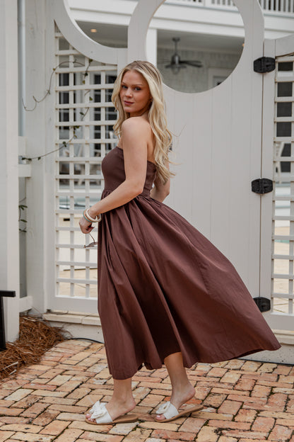Woman in a brown dress standing on a brick patio with white lattice background