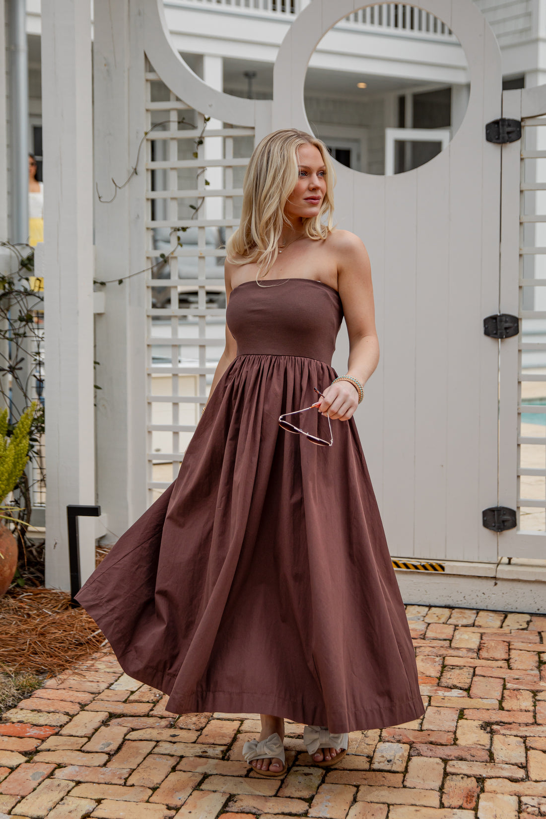 Woman in a brown strapless dress standing in front of a decorative white wall.