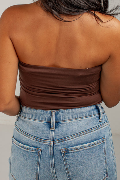 Rear view of a woman wearing a dark brown strapless bandeau top and light blue denim jeans.