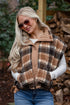 Woman wearing a plaid vest and sunglasses outdoors with stacked firewood in the background