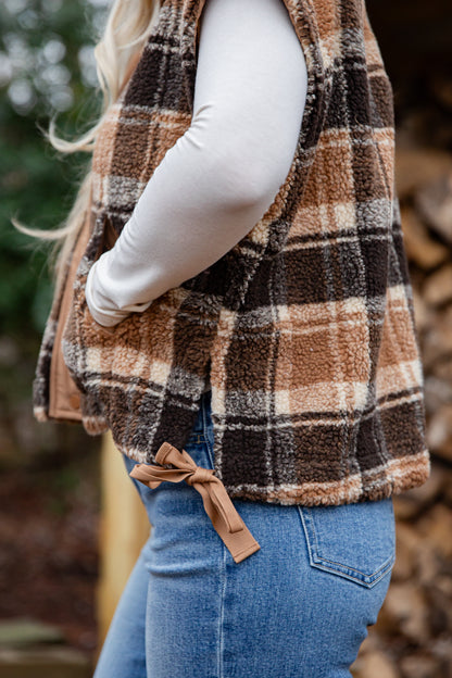 Person wearing a plaid vest with a blurred natural background