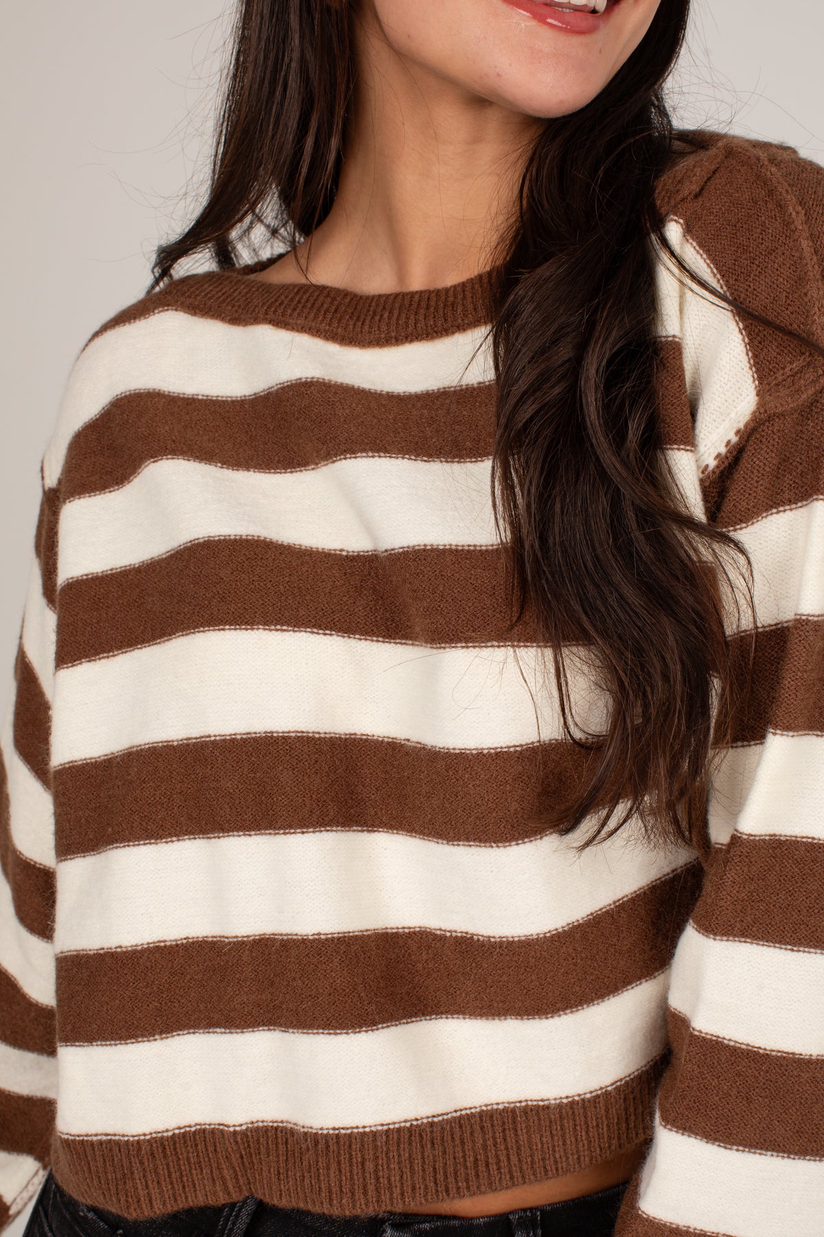 A close-up of a woman wearing a brown and cream striped knit sweater, showing the texture of the fabric and the horizontal stripe pattern.
