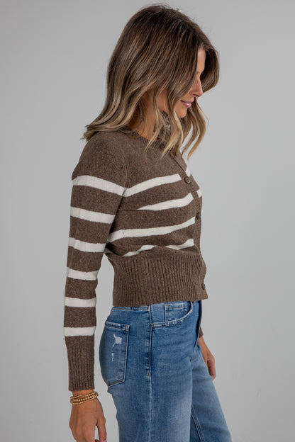 Woman wearing a brown and white striped sweater with blue jeans on a gray background