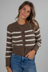 Woman wearing a brown and white striped cardigan with blue jeans on a gray background