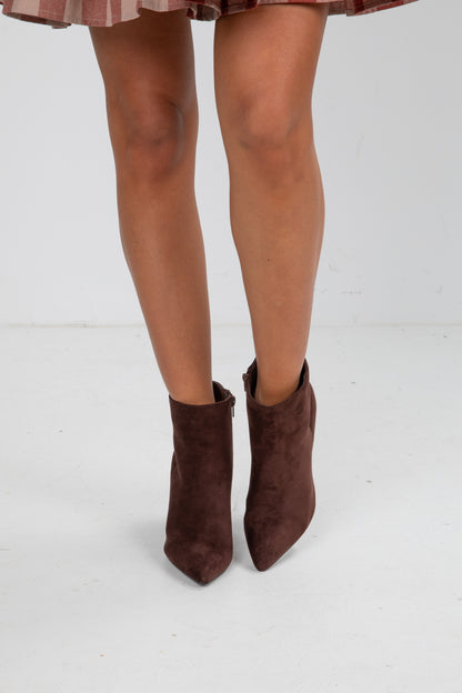 Brown suede ankle boots worn with a plaid skirt on a white background