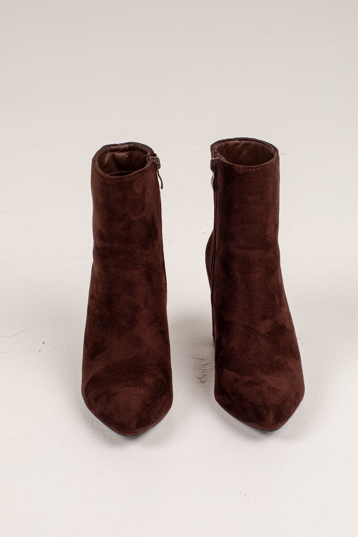 A pair of dark brown suede ankle boots with pointed toes and side zippers, photographed against a plain off-white background.