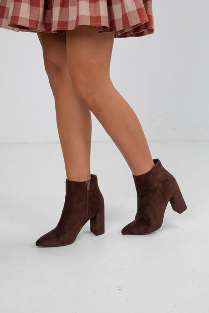 Brown suede ankle boots worn with a red and white checkered skirt on a light gray background