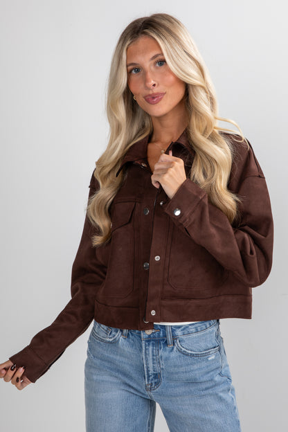 Woman wearing a brown jacket and blue jeans on a plain background