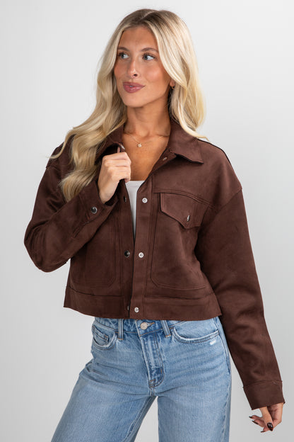 Woman wearing a brown jacket and blue jeans on a plain background