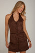 A woman wearing a brown suede-like halter mini dress with front buttons, photographed against a plain off-white wall.