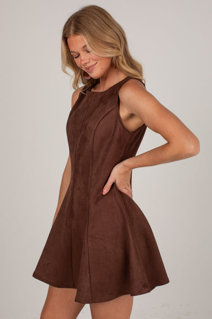 A woman modeling a sleeveless brown skater dress with a flared skirt against a plain light gray studio background.