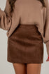 Person wearing a brown sweater and suede skirt on a plain background