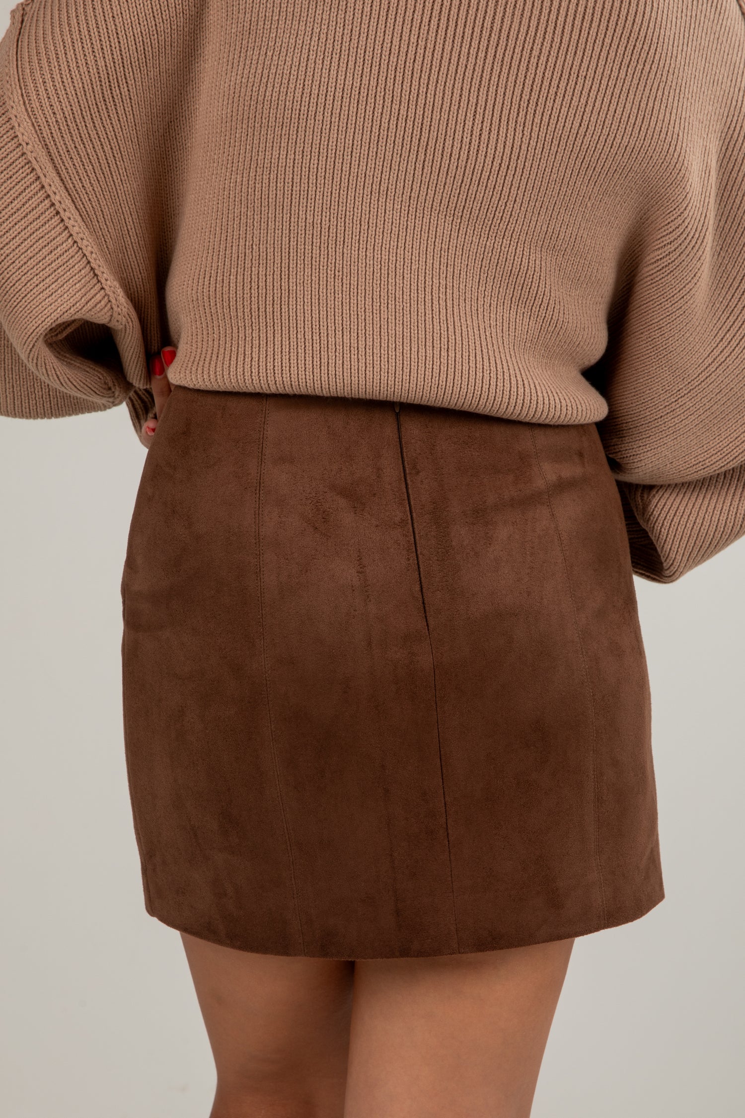 Brown suede skirt worn with a beige sweater on a plain background