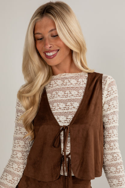 Woman wearing a brown vest over a patterned top against a plain background