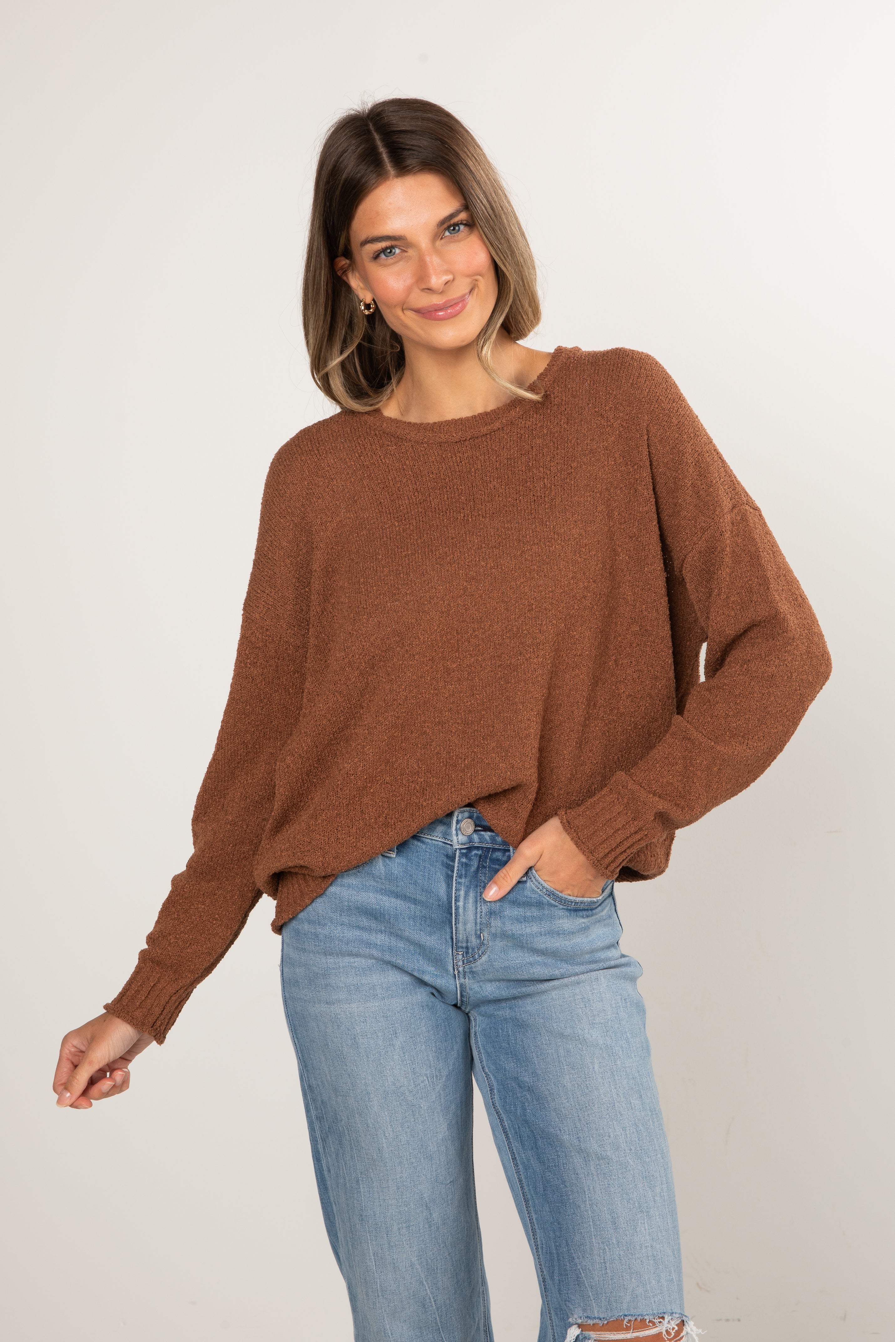 Woman wearing a brown sweater and blue jeans against a white background