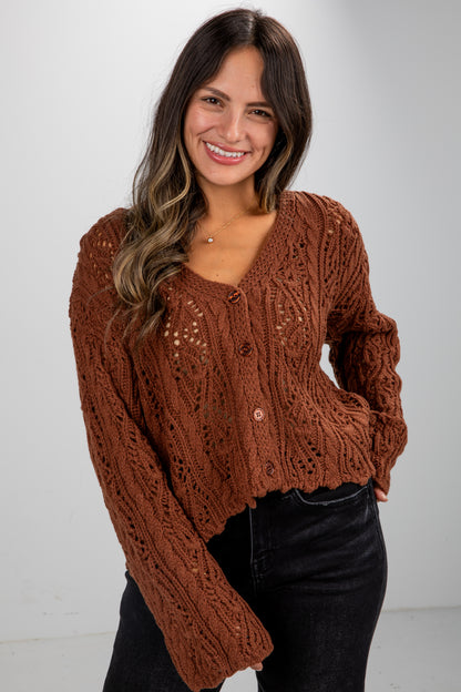 Woman wearing a brown cable knit sweater against a white background