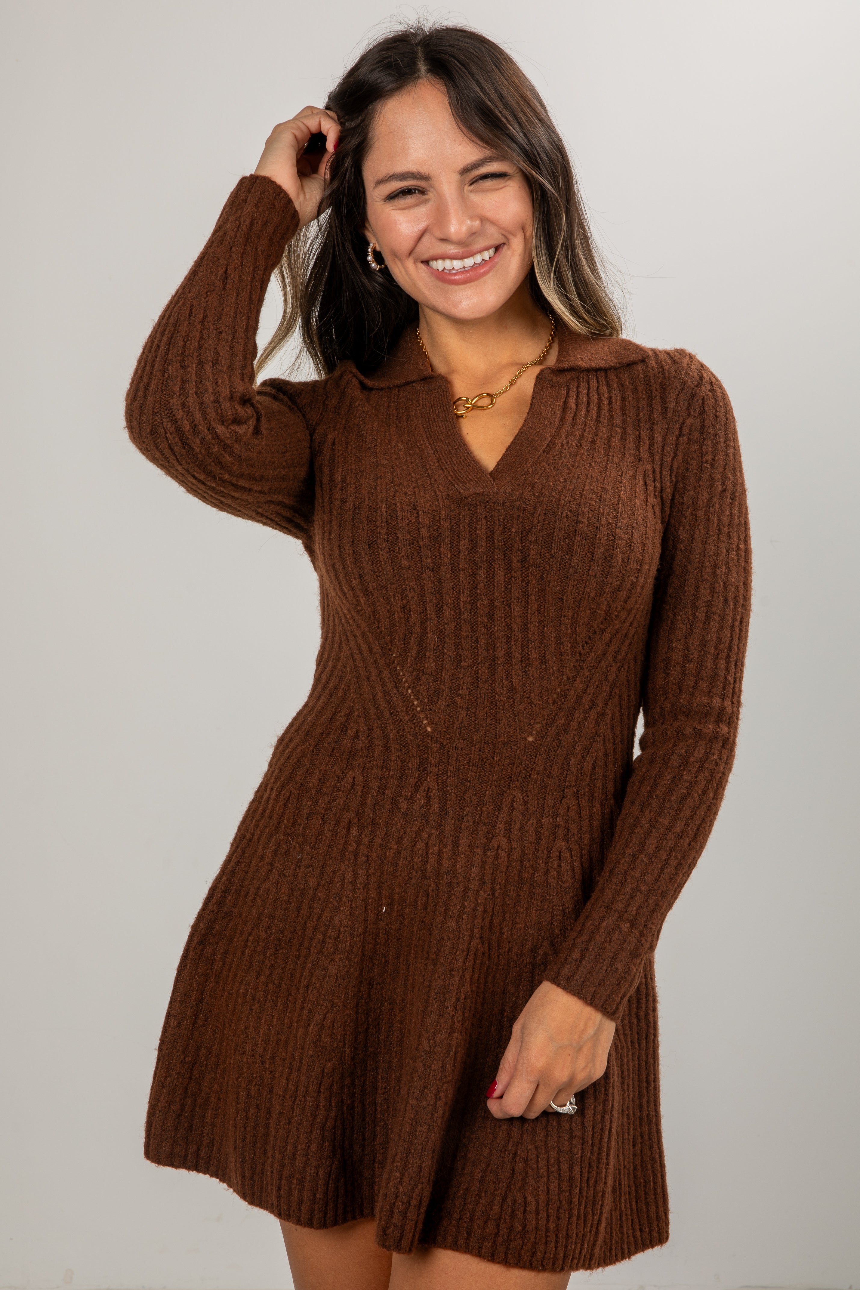 Woman wearing a brown knitted dress against a plain background