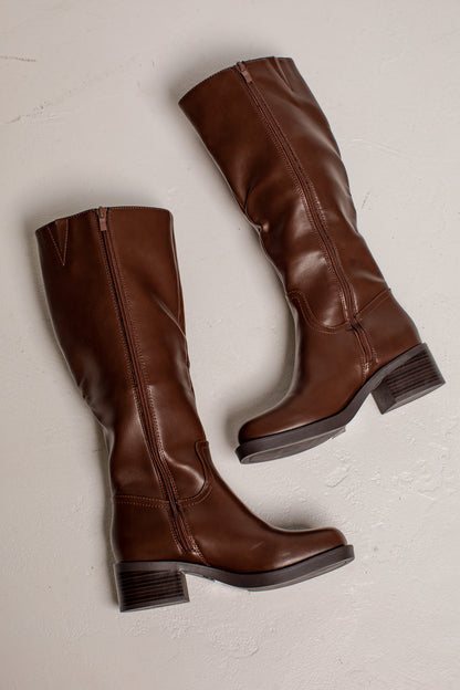 A pair of knee-high brown leather boots with low block heels, shown from a top-down angle on a light textured background.