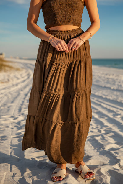 Person wearing a brown dress standing on a sandy beach with ocean in the background