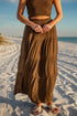 Person wearing a brown dress standing on a sandy beach with ocean in the background