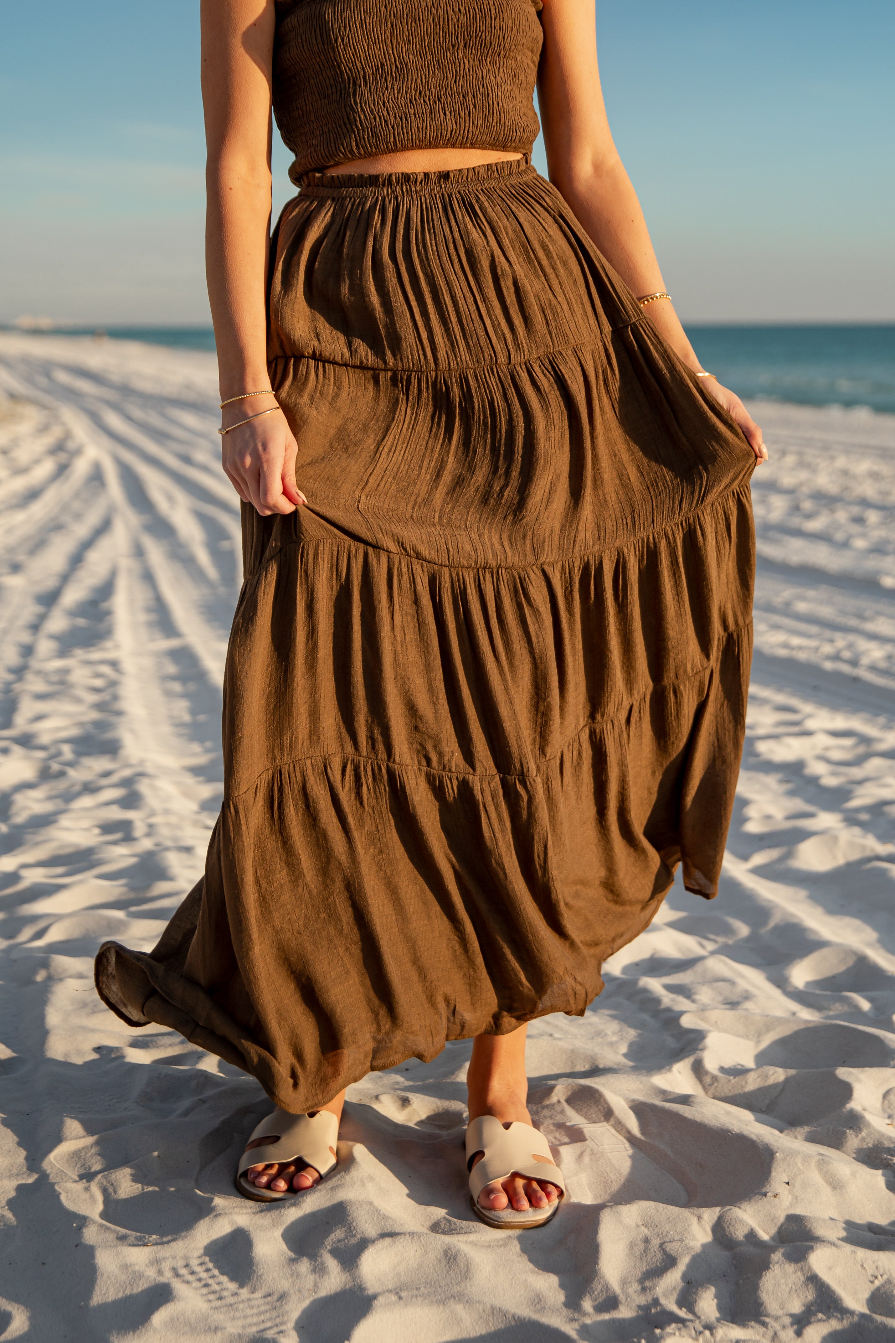 Person wearing a brown dress standing on a sandy beach with ocean view
