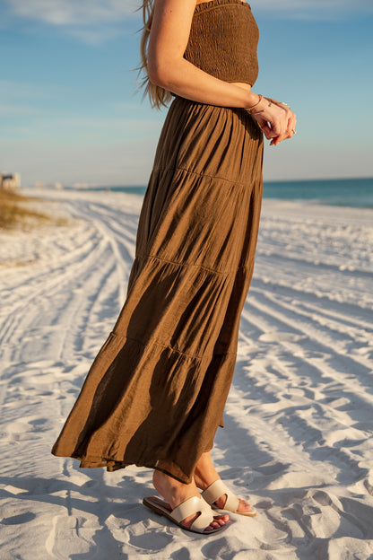 Person wearing a long brown dress on a sandy beach with ocean view