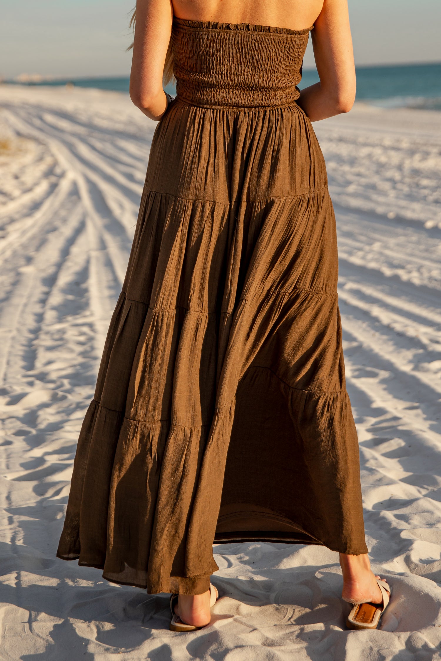 Woman wearing a brown dress standing on a sandy beach with ocean view