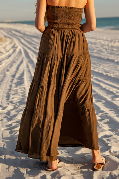 Woman wearing a brown dress standing on a sandy beach with ocean view
