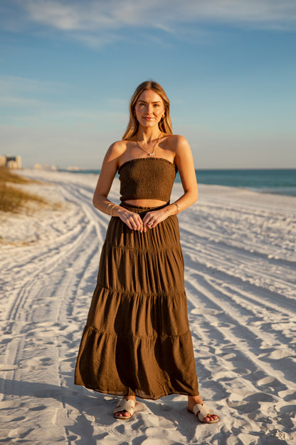 Woman in a brown dress standing on a sandy beach with ocean and sky in the background