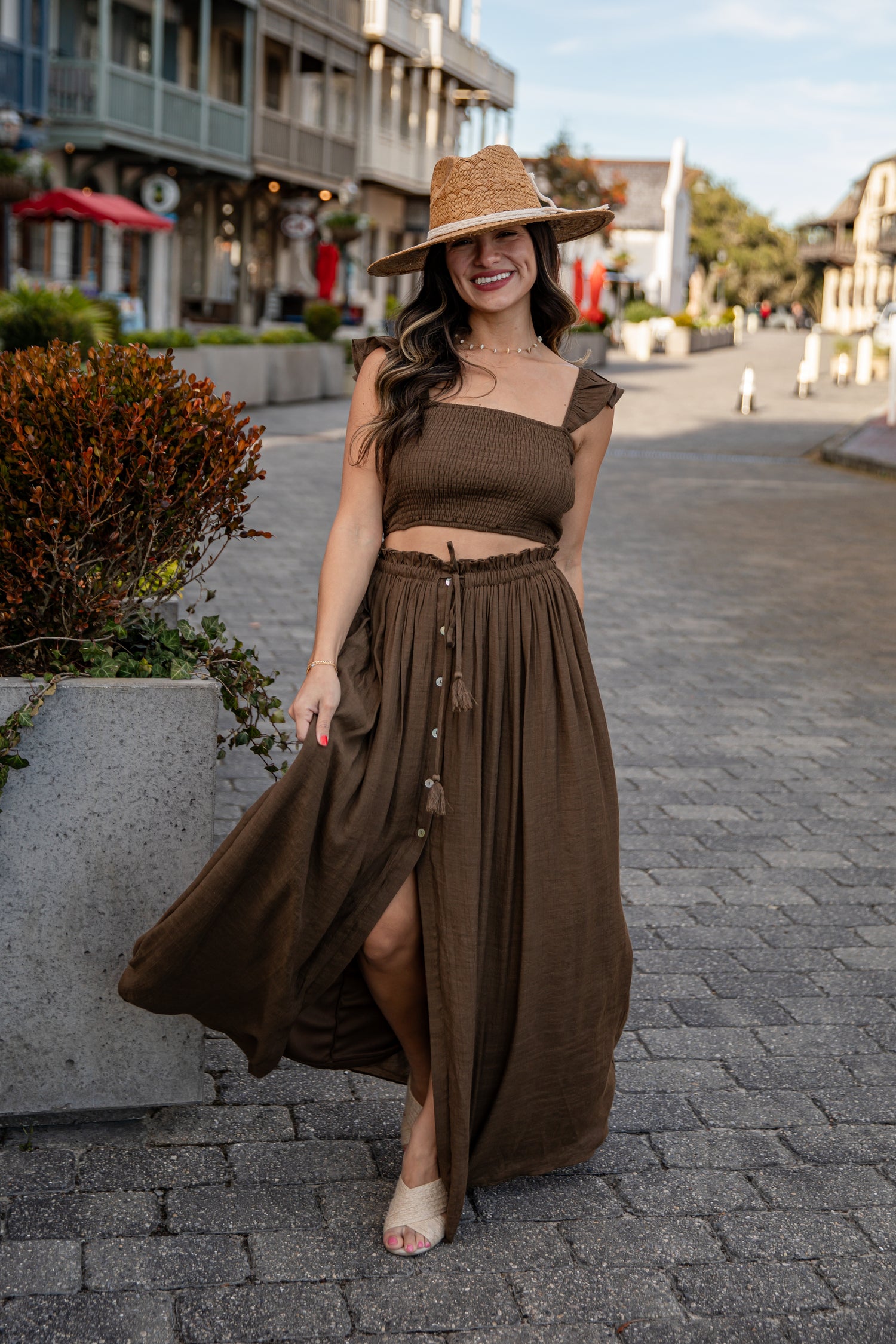 Woman in a brown outfit with a hat standing on a street