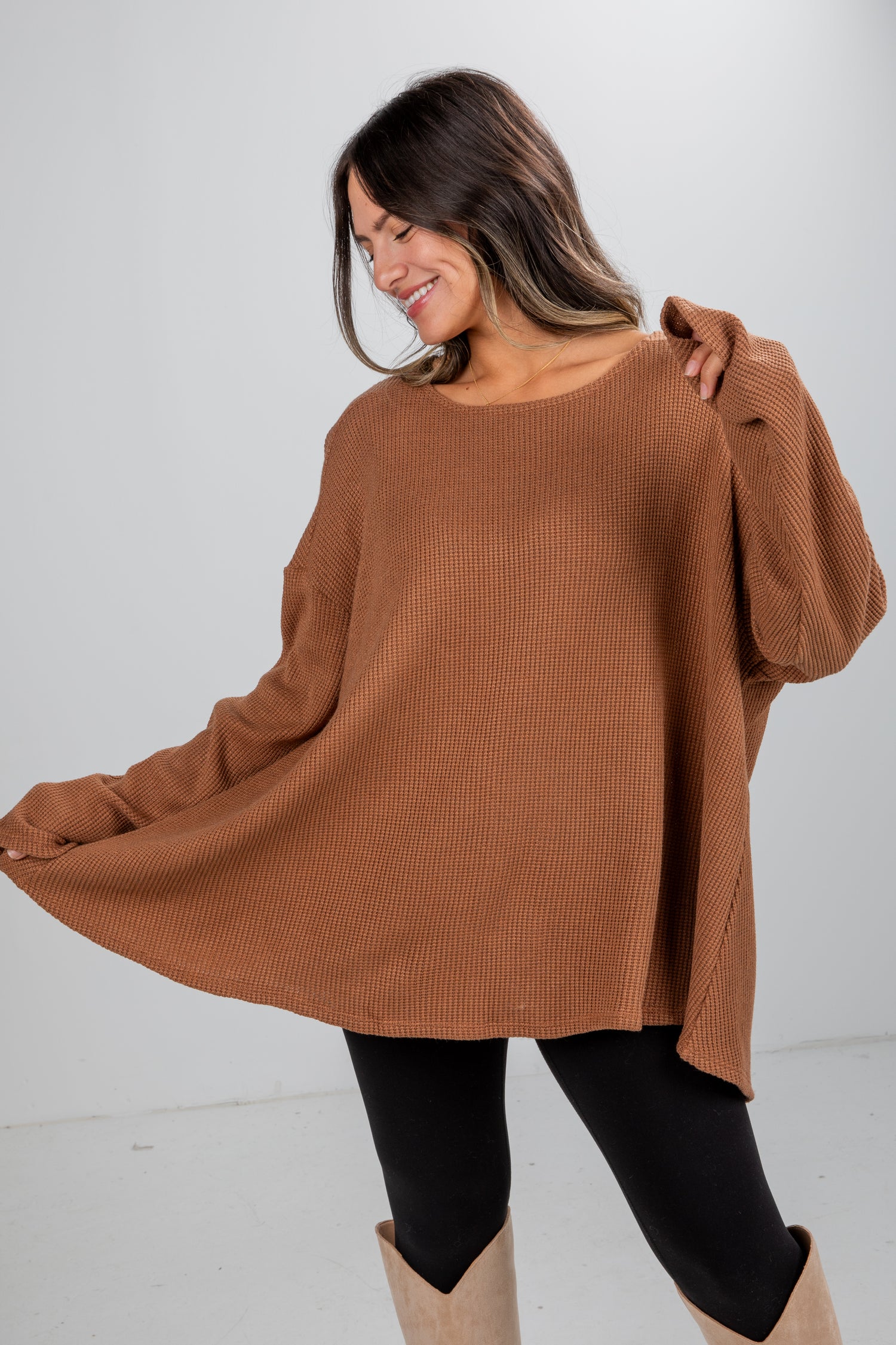 Woman wearing a brown sweater and black leggings on a white background