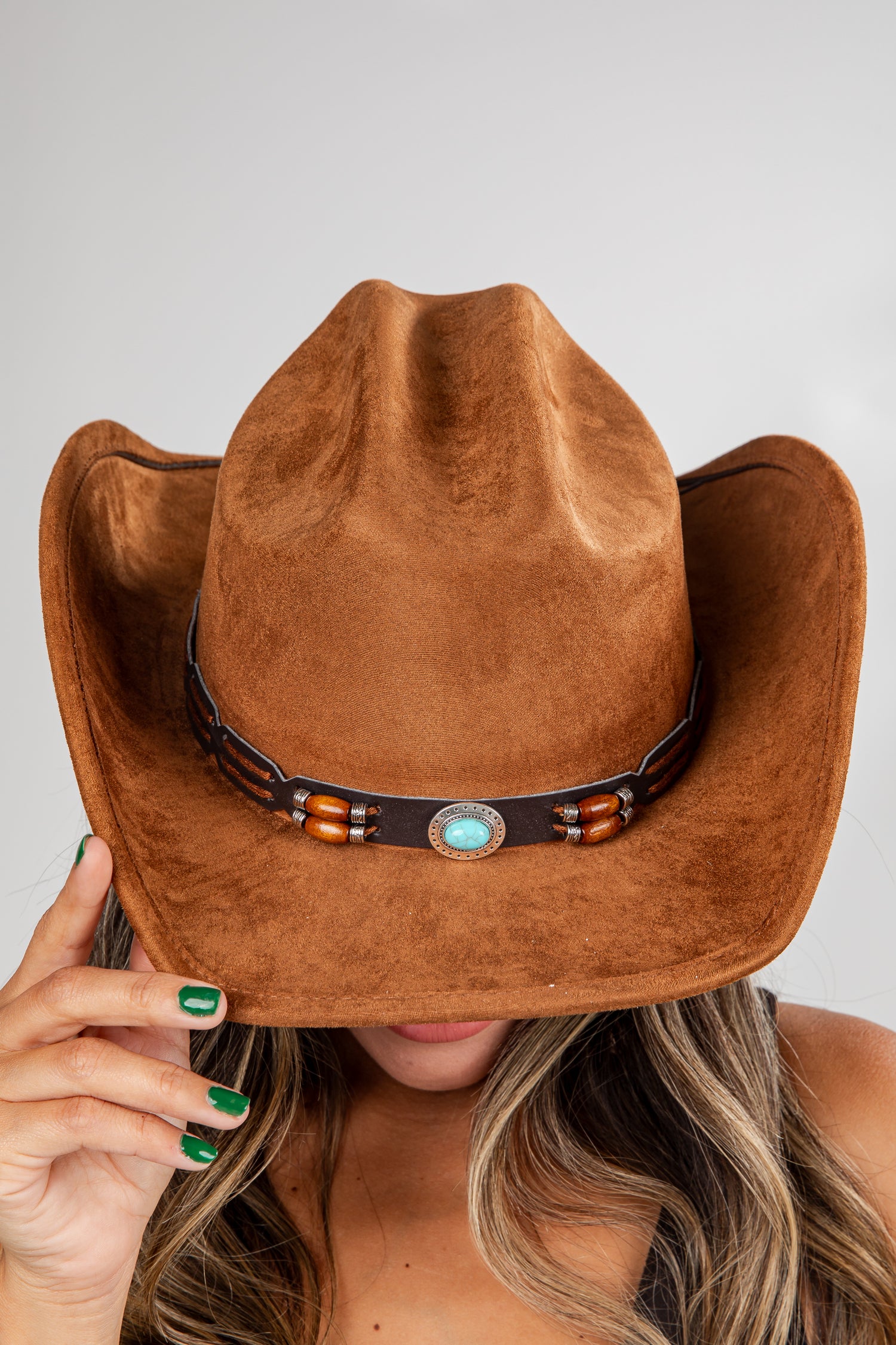 Brown cowboy hat with a decorative band held by a person against a neutral background