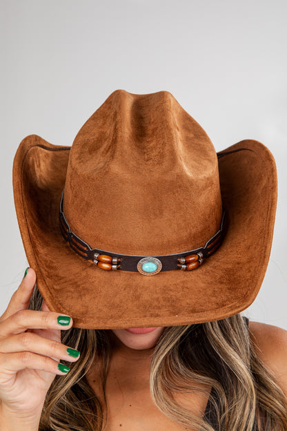 Brown cowboy hat with a decorative band held by a person against a neutral background