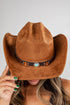Brown cowboy hat with a decorative band held by a person against a neutral background