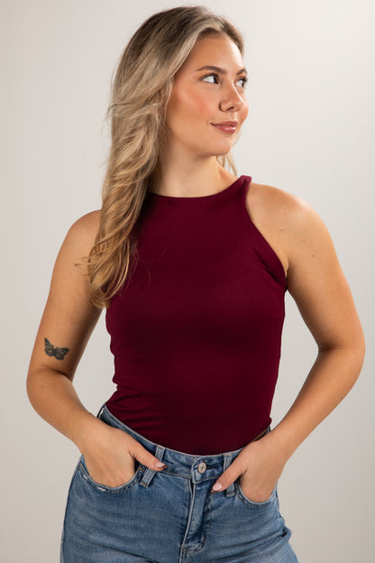 Woman wearing a burgundy sleeveless top and blue jeans against a plain background