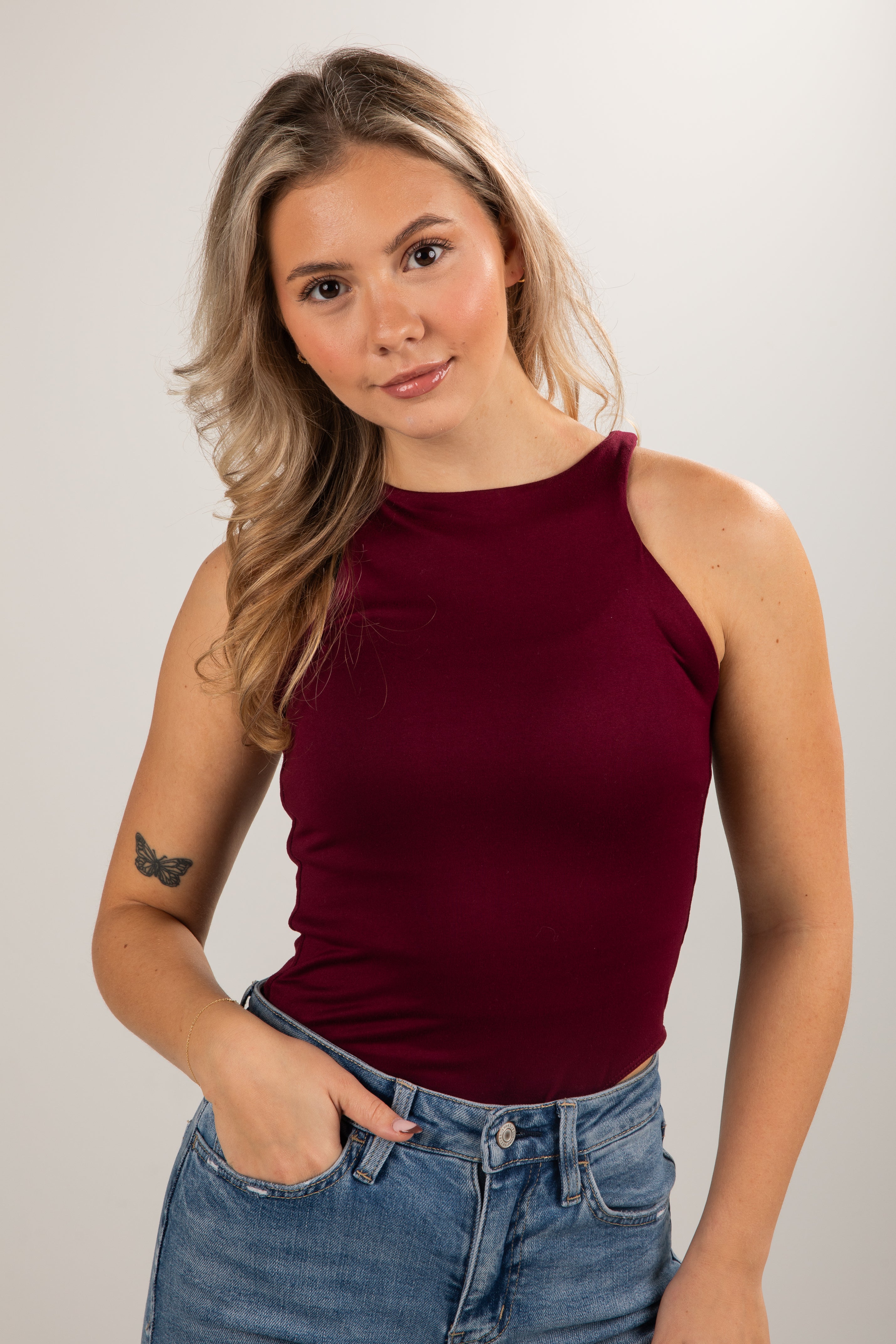 Woman wearing a burgundy tank top and blue jeans against a plain background