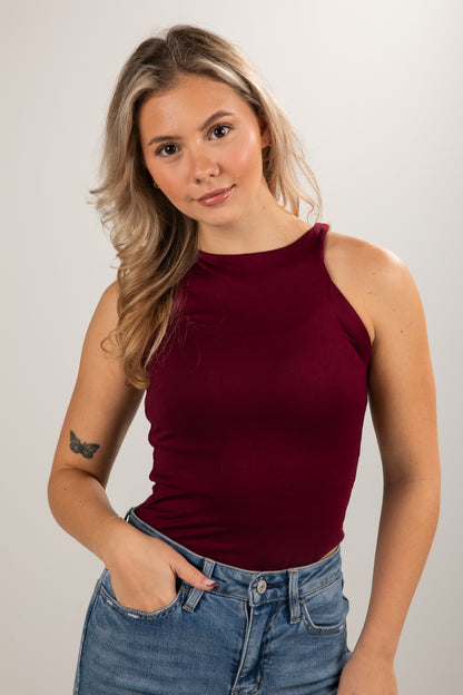 Woman wearing a burgundy tank top and blue jeans against a plain background