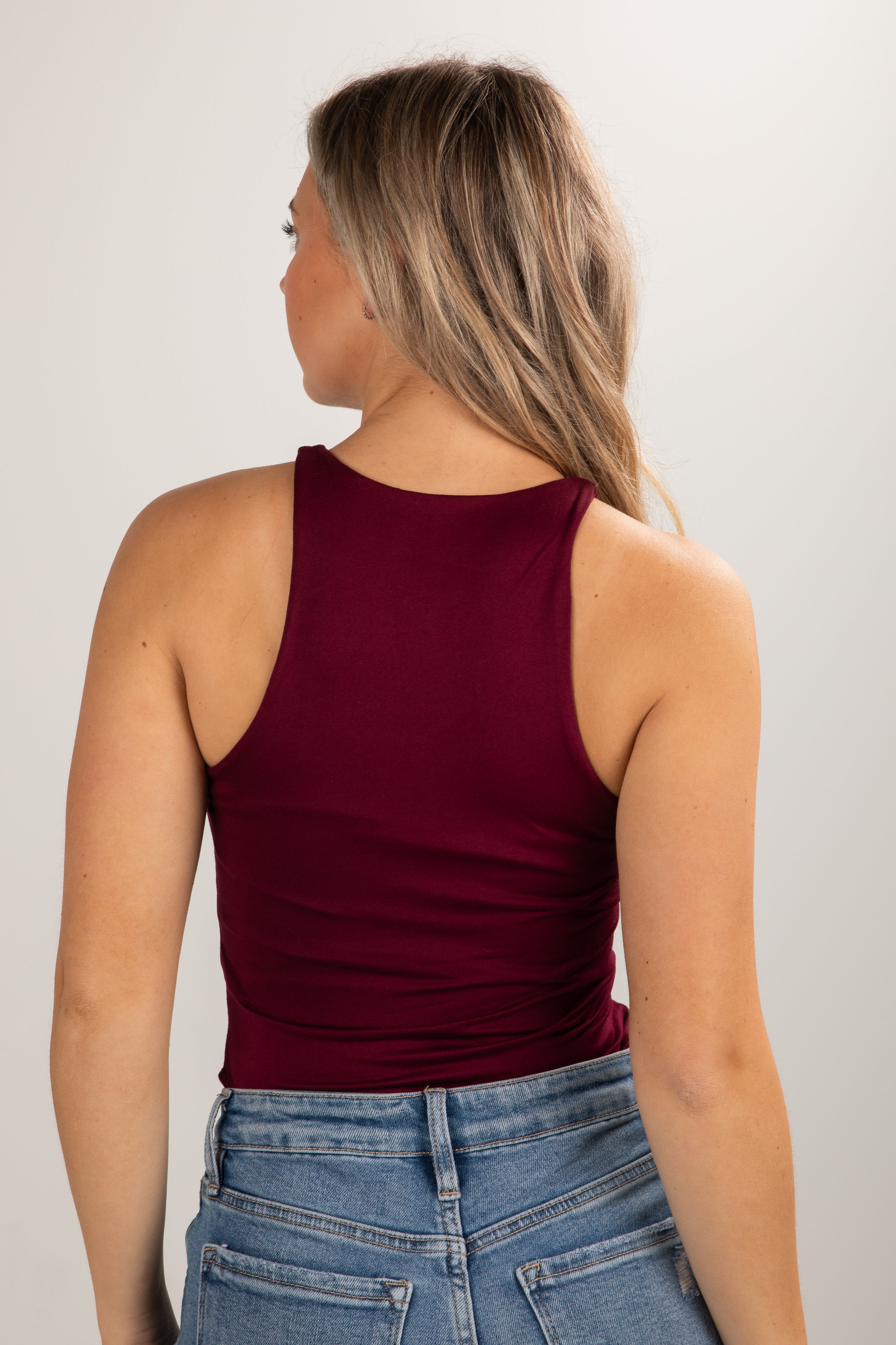 Woman wearing a burgundy tank top and blue jeans against a white background