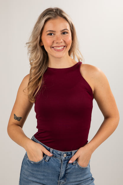 Woman wearing a burgundy sleeveless top and blue jeans against a plain background