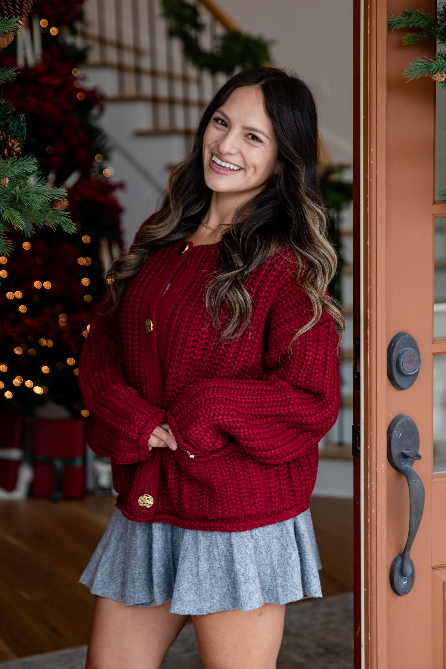 Woman wearing a red sweater and blue skirt standing in front of a decorated Christmas tree.