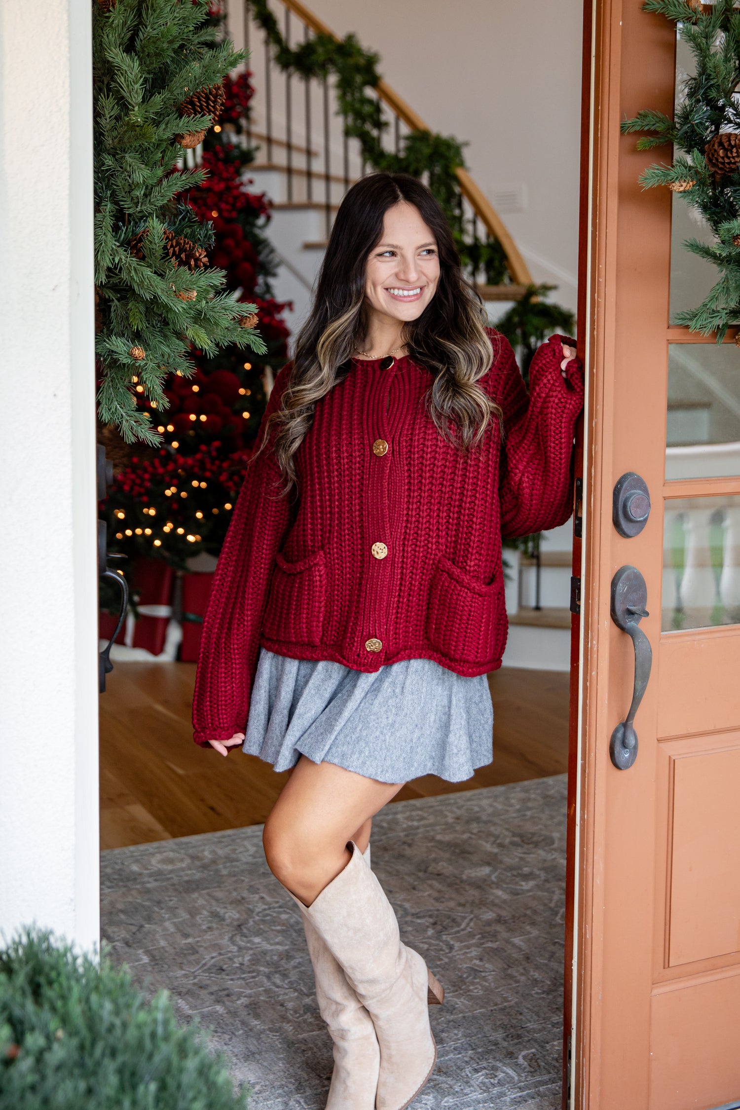 Woman in a red cardigan and blue skirt standing in a doorway with Christmas decorations.