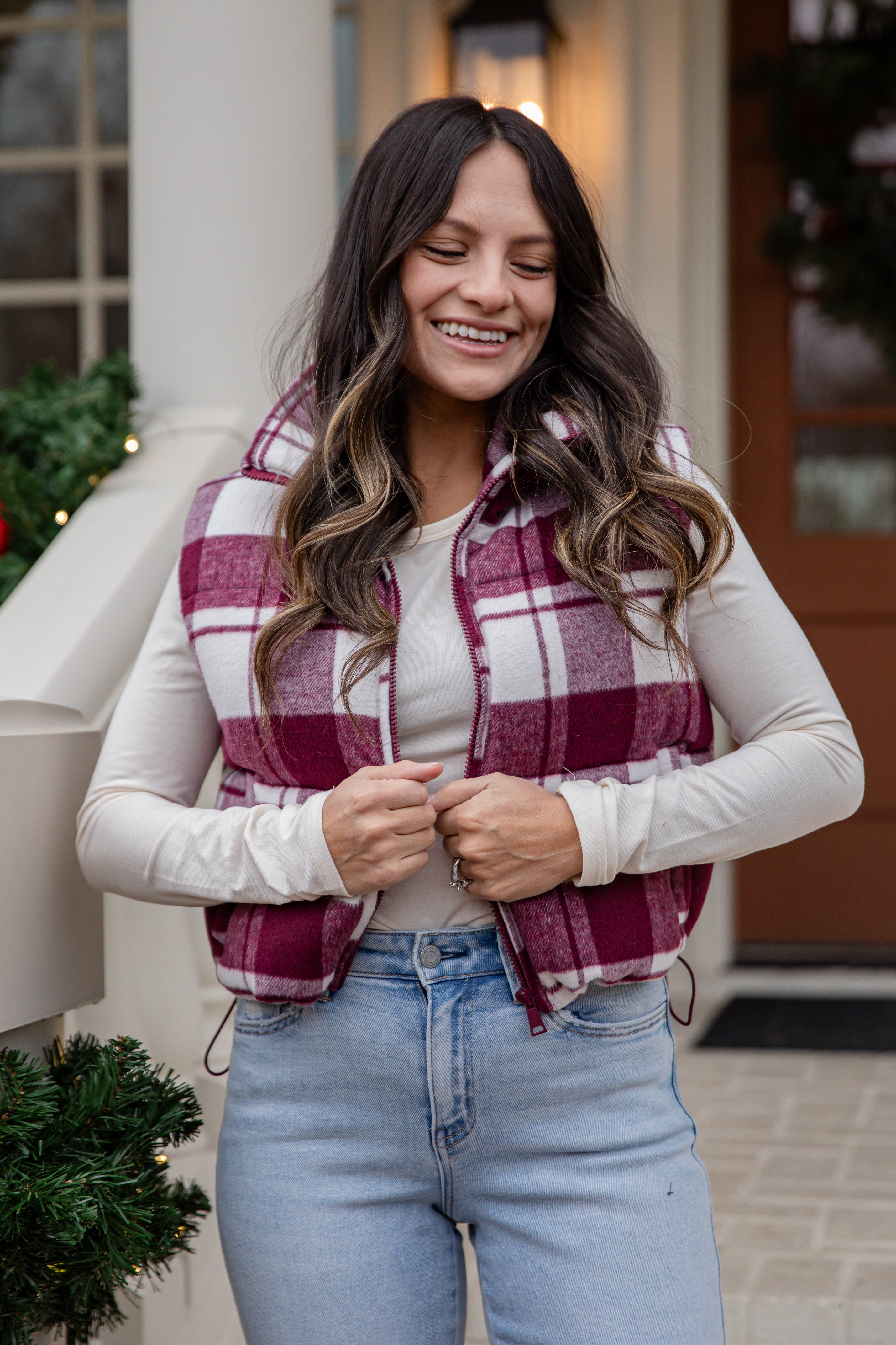 Woman wearing a plaid vest, white shirt, and blue jeans standing outdoors.