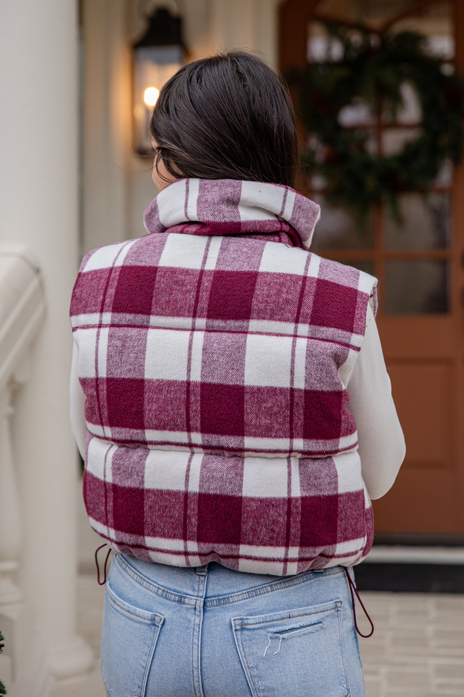 Person wearing a plaid puffer vest in front of a door with a wreath.