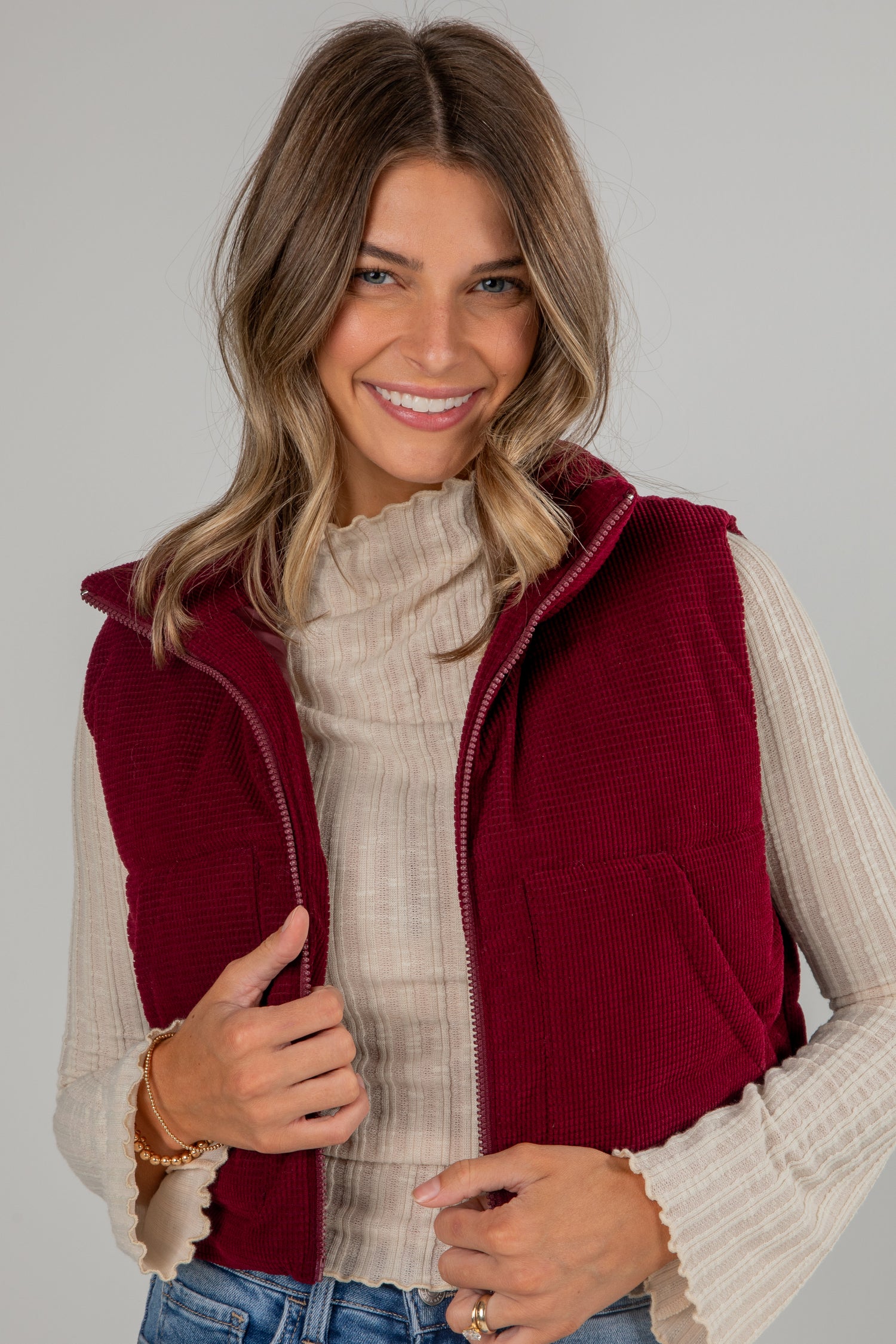 Woman wearing a red vest over a beige sweater on a plain background