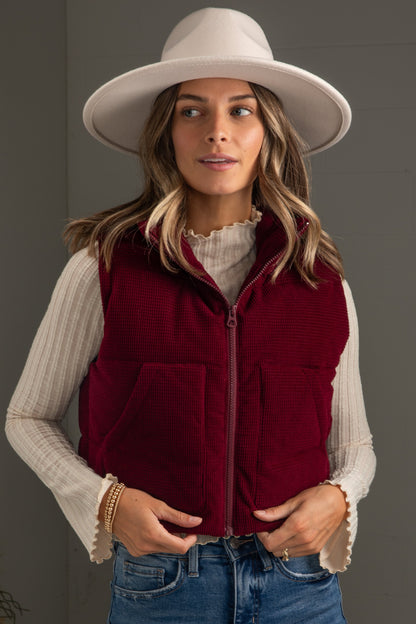Woman wearing a red vest, white hat, and blue jeans against a gray background